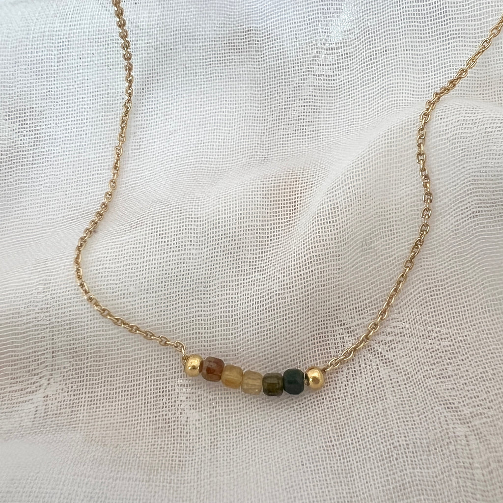 Necklace with small beads on a gold chain against a textured white background