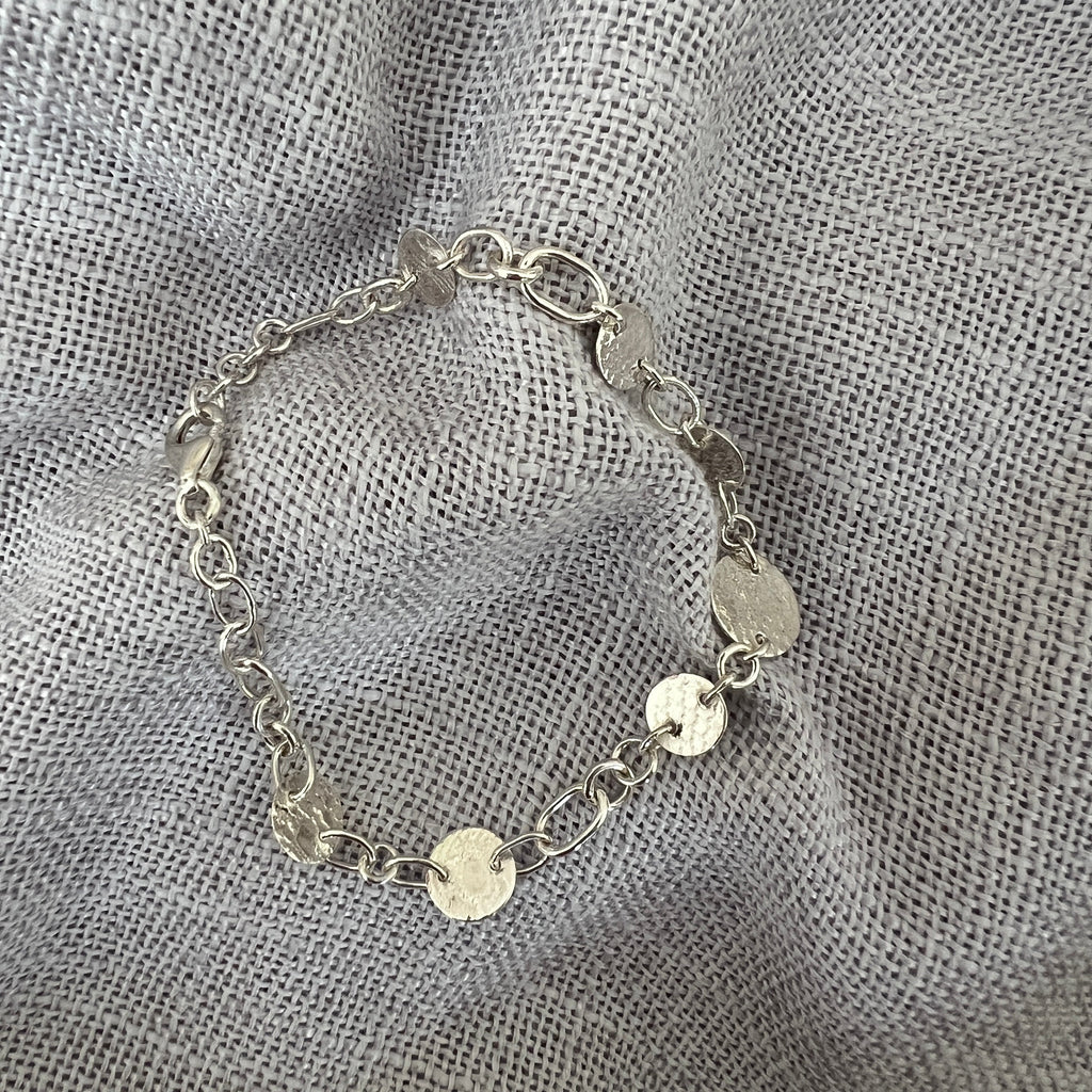 Silver bracelet with circular charms on a textured gray fabric background