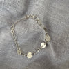 Silver bracelet with circular charms on a textured gray fabric background