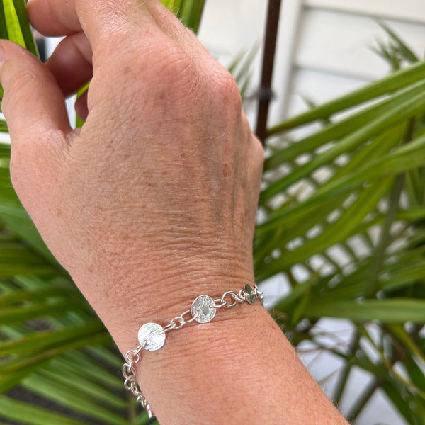 Hand wearing a silver bracelet with greenery in the background