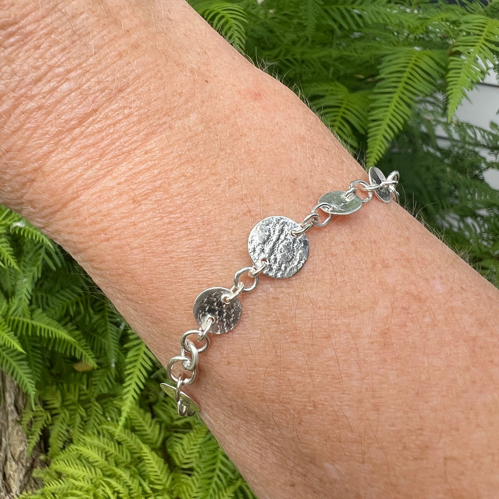 Silver bracelet on a wrist with a green leafy background