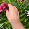 Hand with a silver bracelet touching pink flowers among green leaves