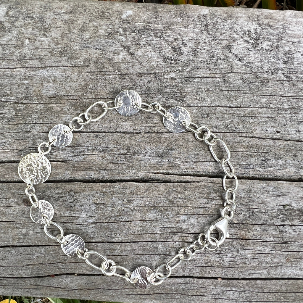 Silver chain necklace on a wooden surface with grass in the background