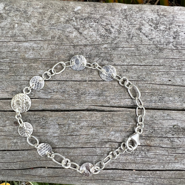Silver chain necklace on a wooden surface with grass in the background