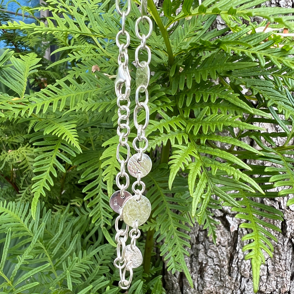Silver bracelet with circular charms on a background of green ferns and tree bark