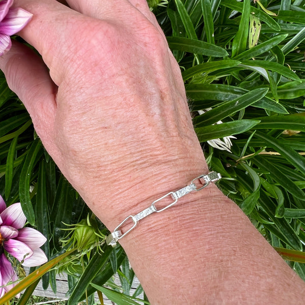 Hand wearing a silver bracelet with green foliage in the background