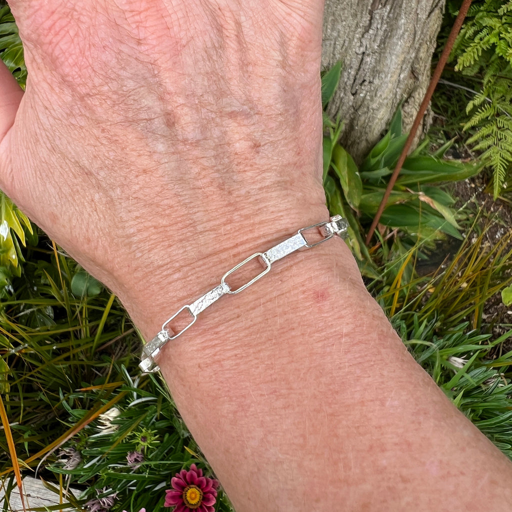 Silver bracelet on a wrist with a natural background of plants and flowers