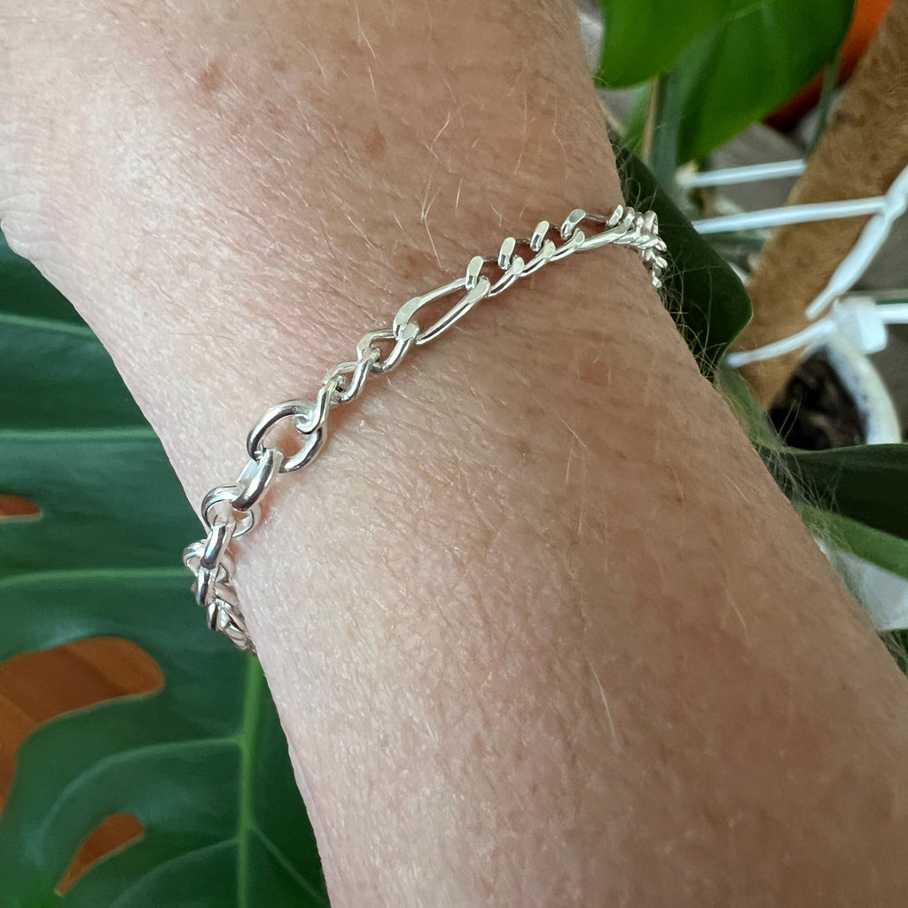Silver chain bracelet on a wrist with a green leafy background