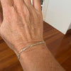 Hand wearing a silver chain bracelet on a wooden floor.