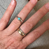 Close-up of a hand wearing two rings with a turquoise stone on a textured surface