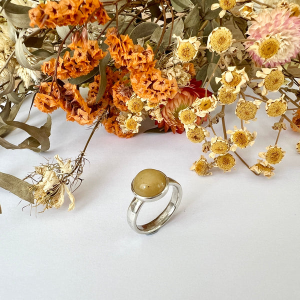 Silver ring with a round stone on a white background with dried flowers.