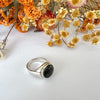 Silver ring with a black stone on a white background with dried flowers.