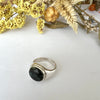Silver ring with a dark stone on a white surface with dried flowers.