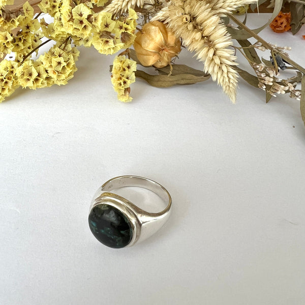 Silver ring with a dark stone on a white surface with dried flowers.
