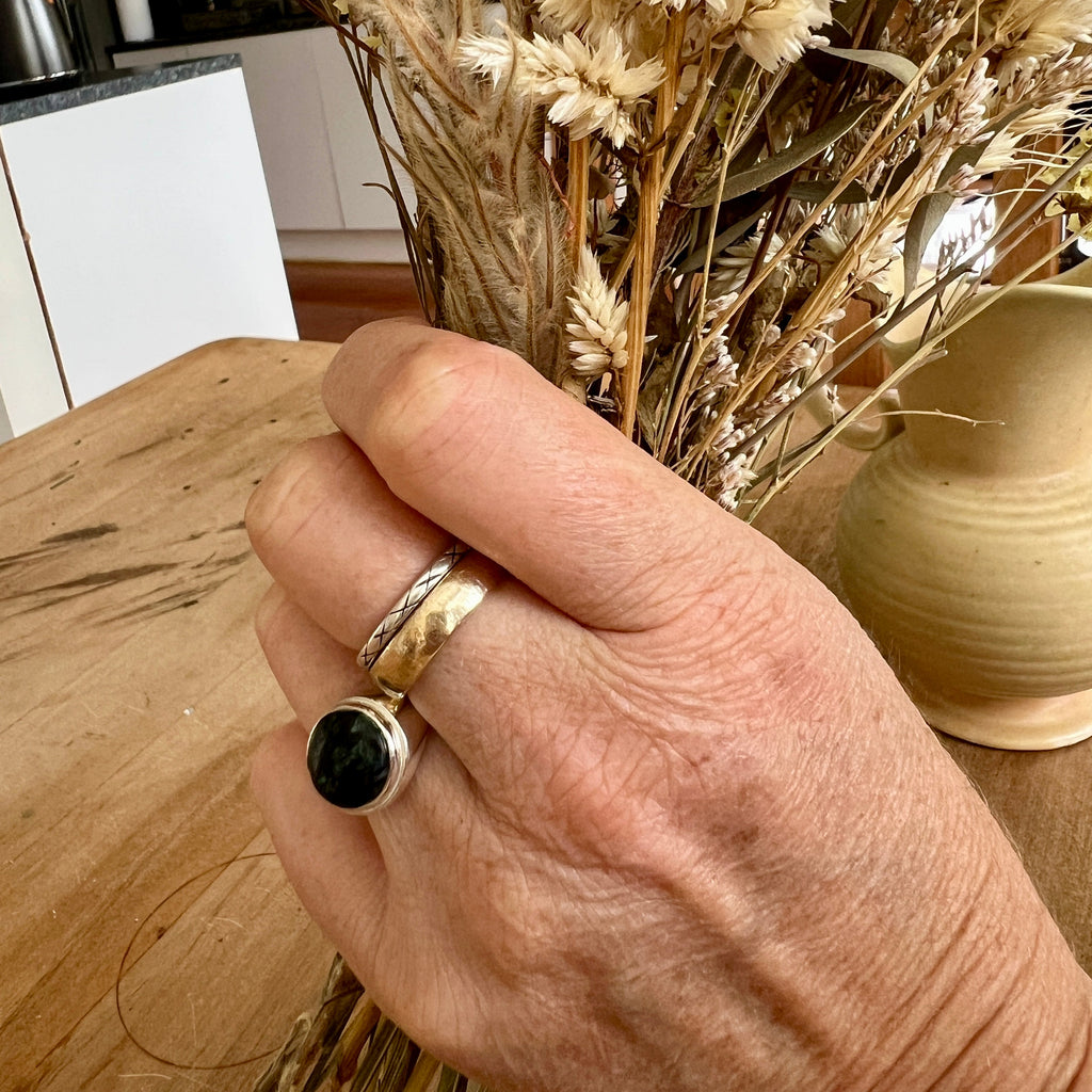 Hand wearing a ring with a black stone, holding dried flowers on a wooden surface.