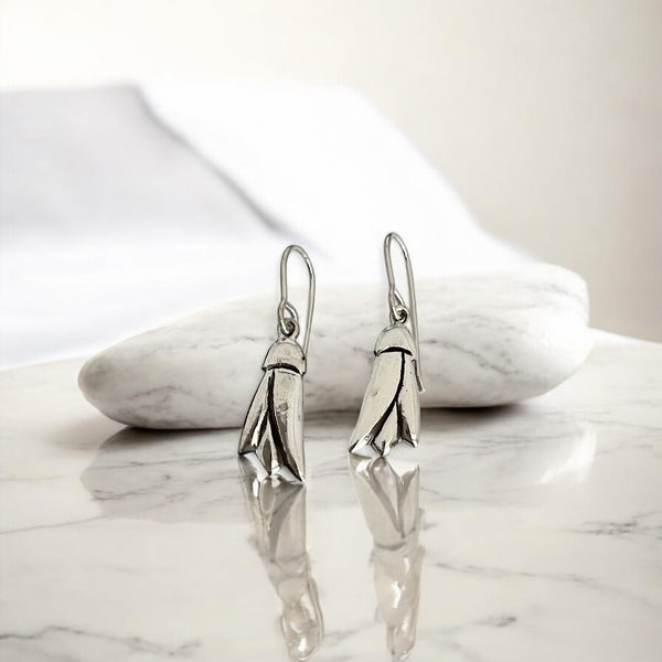 Silver Kowhai flower earrings on a marble surface