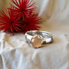 Silver ring with a peach-colored stone on a white fabric background with red floral elements.