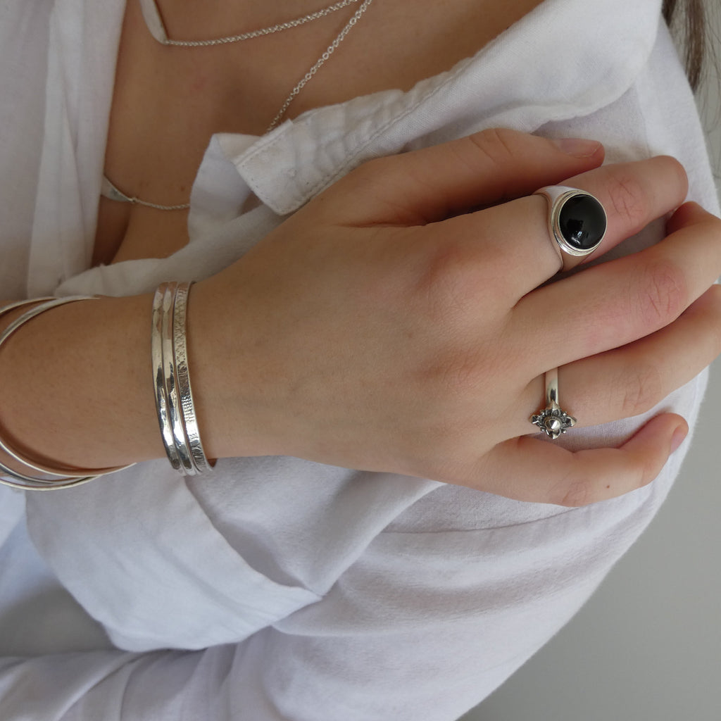 Close-up of a person's hand wearing multiple silver rings and bracelets on a plain background