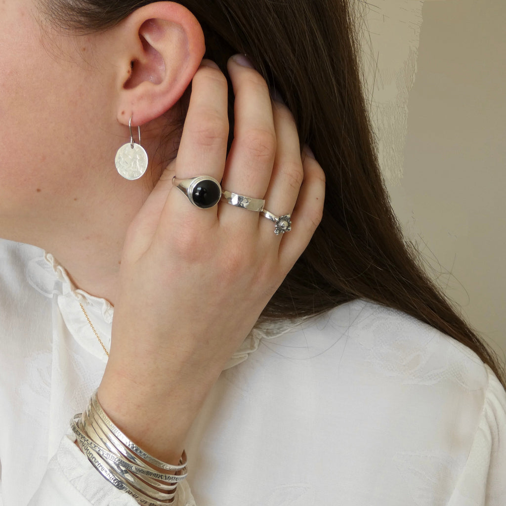 Close-up of a person wearing silver earrings, ring, and bracelets on a neutral background