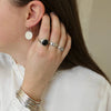 Close-up of a person wearing silver earrings, ring, and bracelets on a neutral background