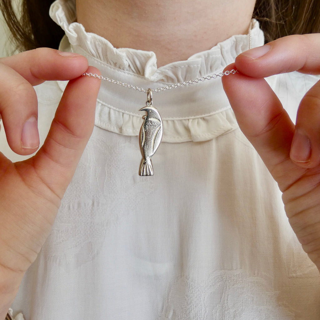Close-up of a silver tui necklace with a pendant held by hands against a blurred background