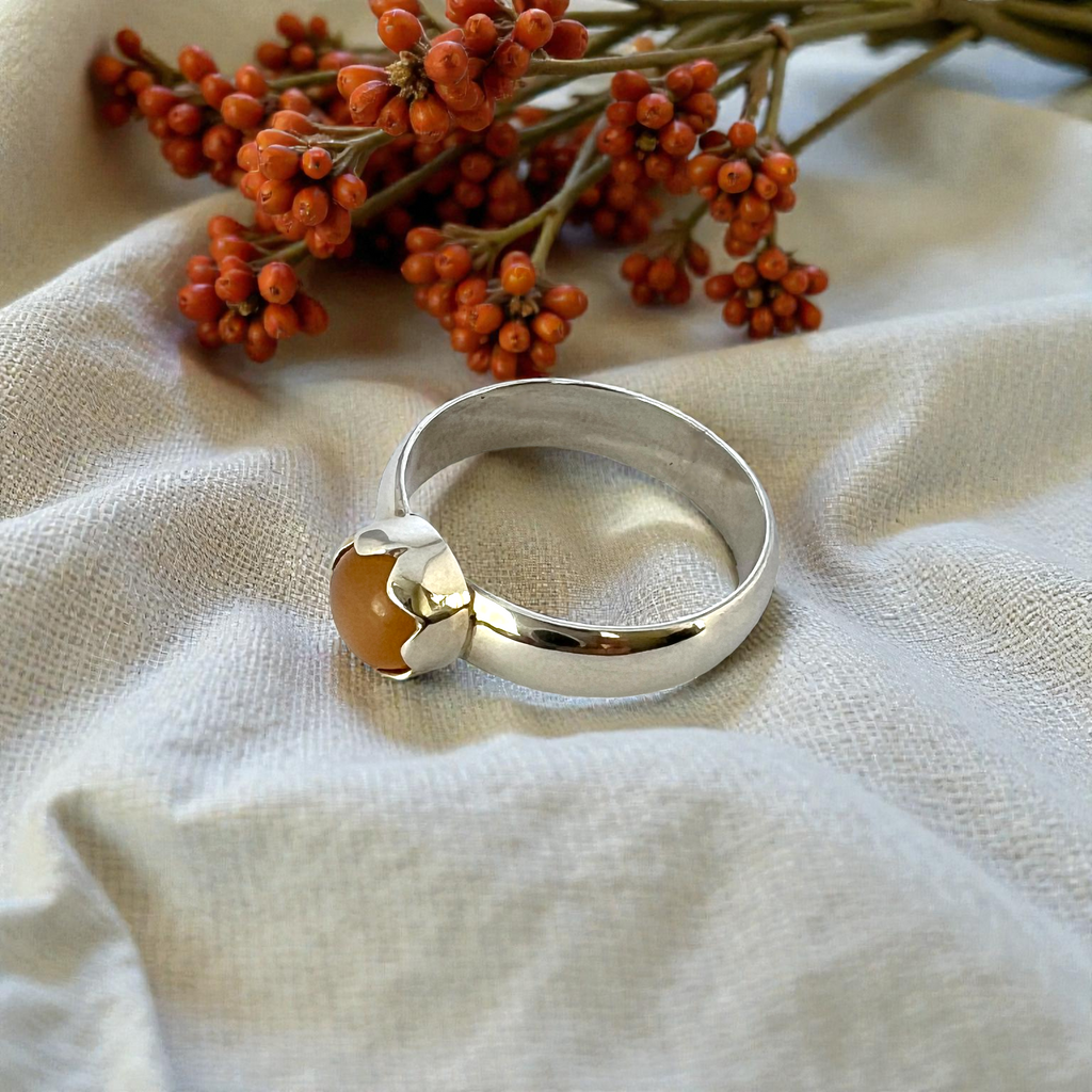 Silver ring with a brown stone on a beige fabric background