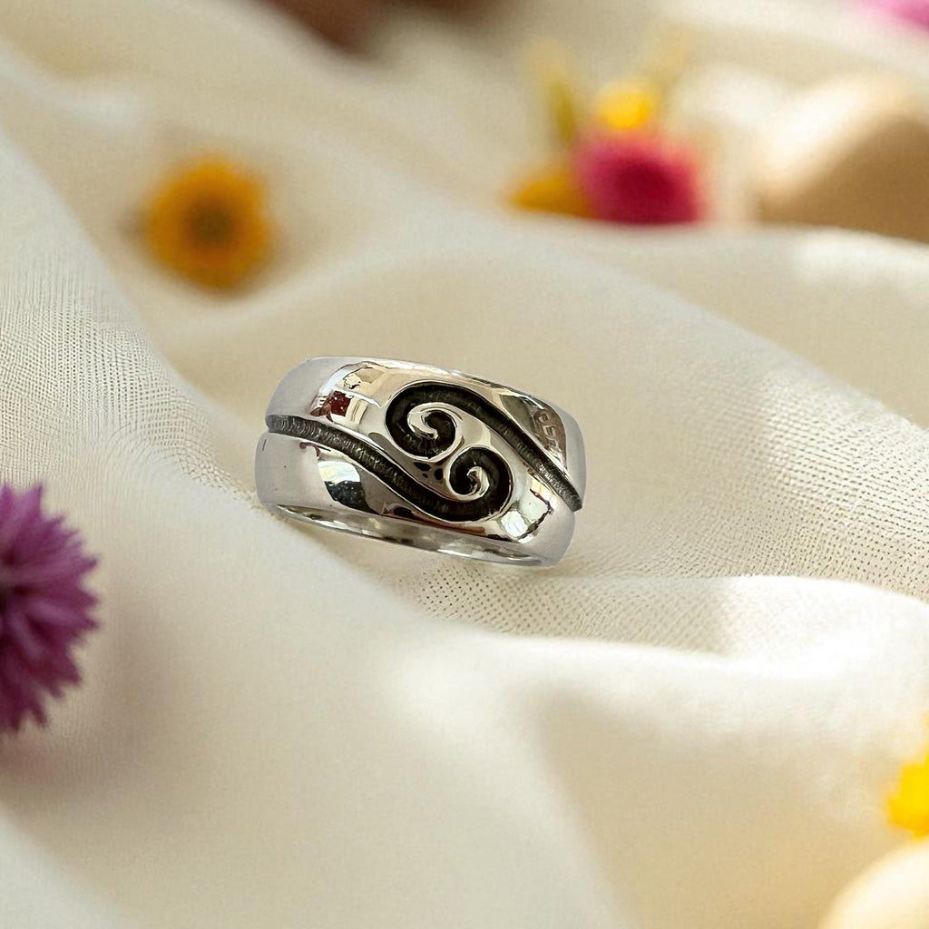 Silver ring with a decorative design on a light fabric background with flowers.