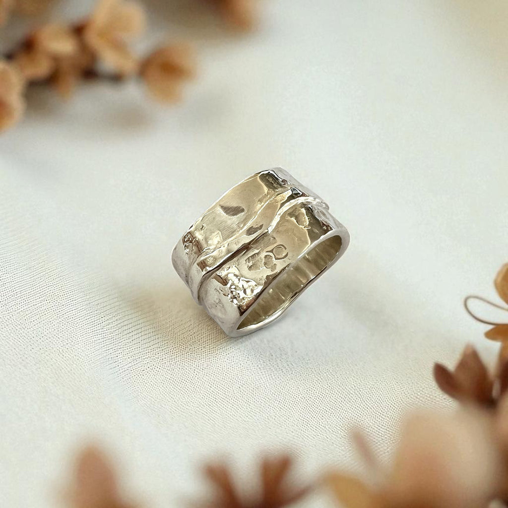 Silver ring with intricate design on a light fabric background with dried flowers