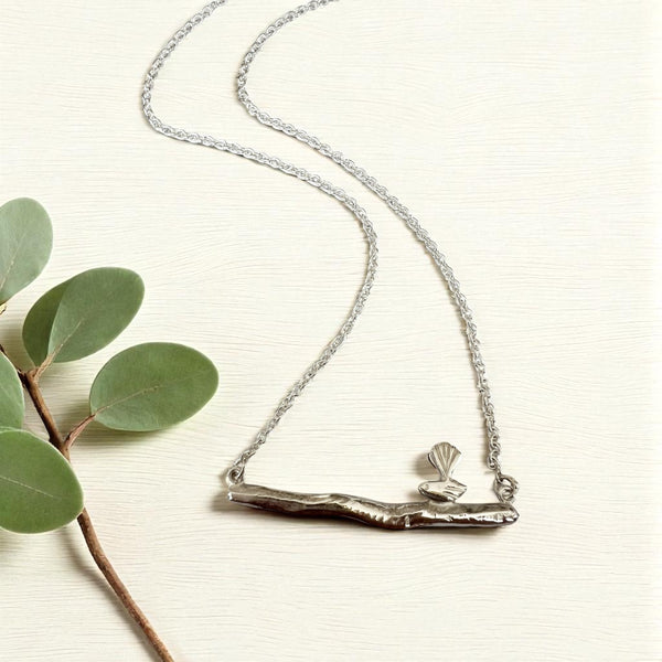 Silver necklace with a bird on a branch-like pendant on a light background