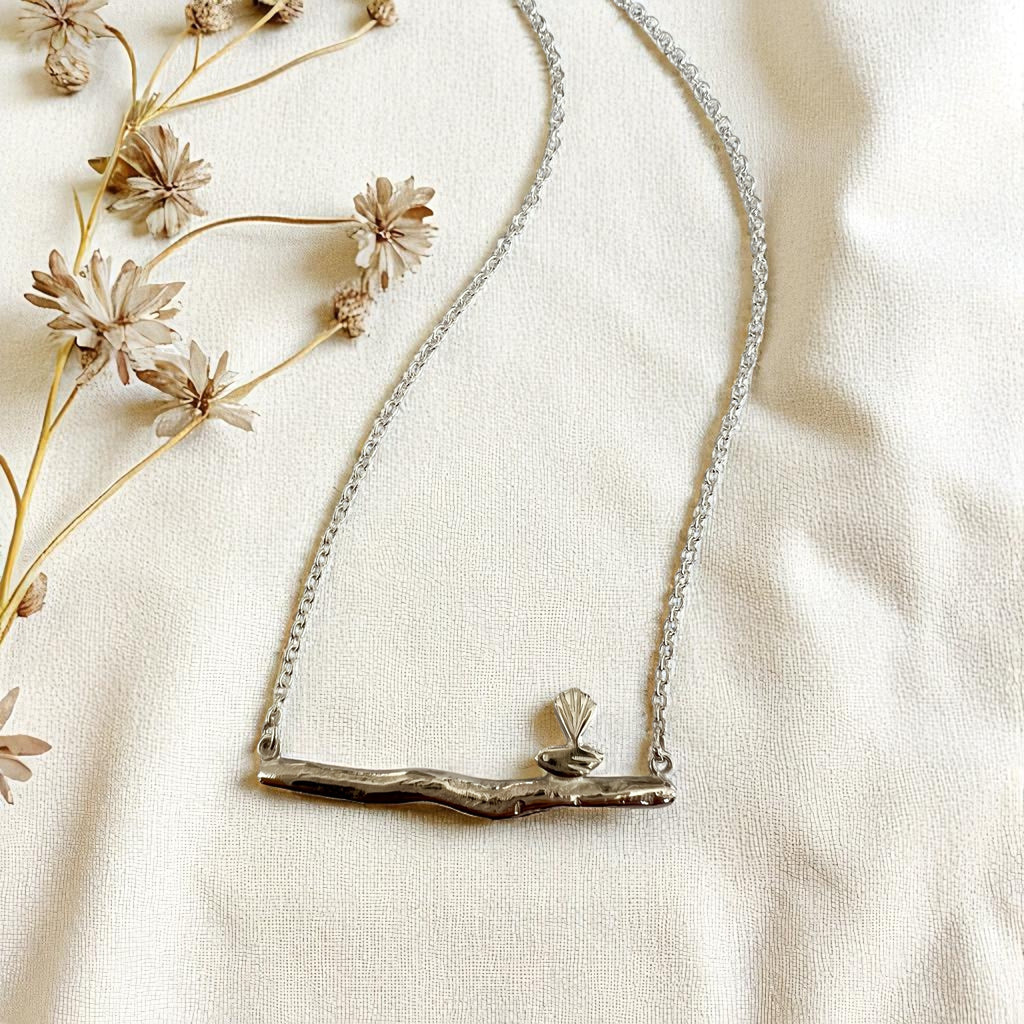 Silver necklace with a bird on branch-like design on a light fabric background