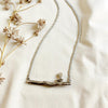 Silver necklace with a bird on branch-like design on a light fabric background