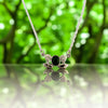 Silver necklace with a green gemstone pendant on a reflective surface with a blurred green background