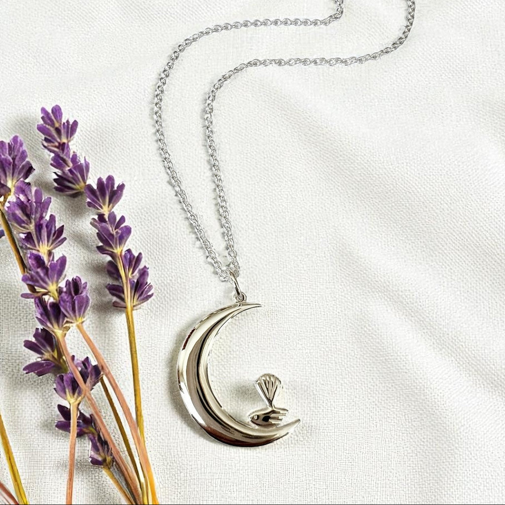 Silver necklace with a crescent moon  pendant on a white background with lavender flowers.