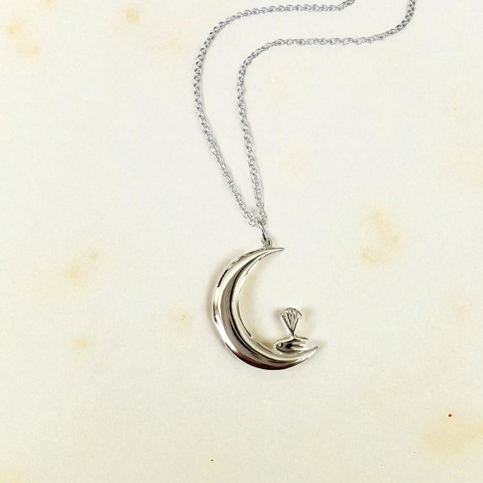 Silver necklace with a crescent moon and bird pendant on a light background