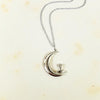 Silver necklace with a crescent moon and bird pendant on a light background