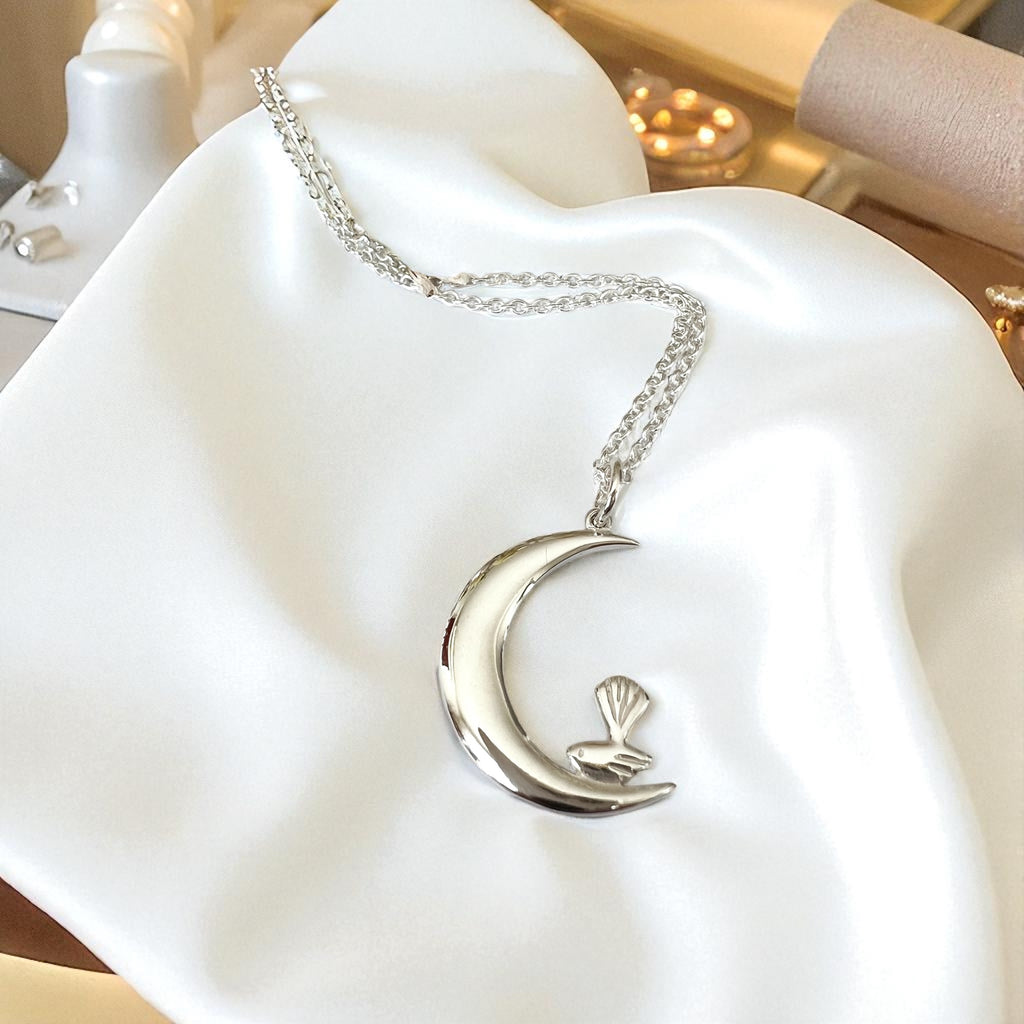 Silver necklace with a moon and bird pendant on a white surface
