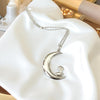 Silver necklace with a moon and bird pendant on a white surface
