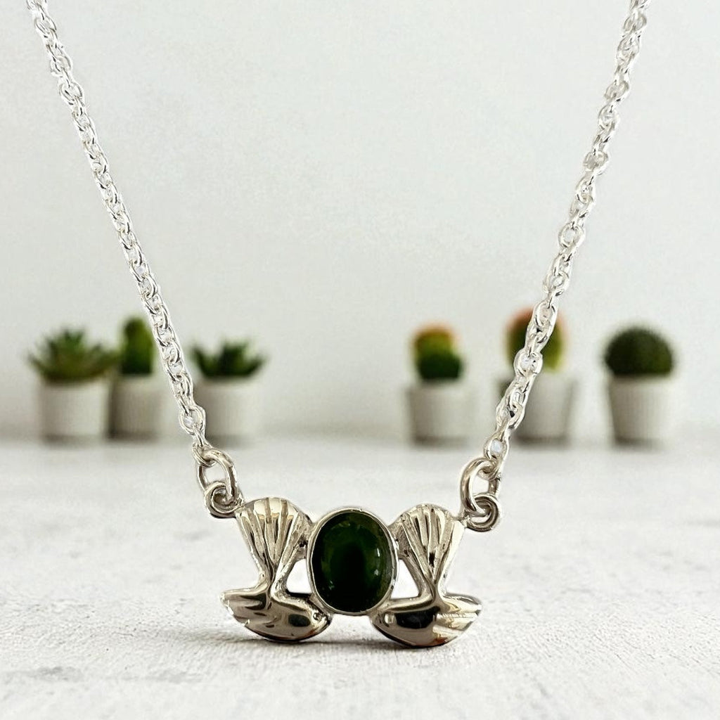 Silver necklace with a green stone pendant on a white surface with blurred plants in the background