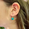 Close-up of an ear wearing a turquoise  earring with silver four claw setting.