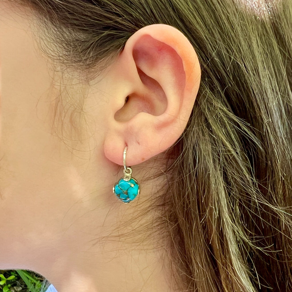 Close-up of an ear wearing a turquoise  earring with silver four claw setting.