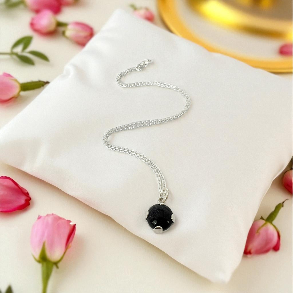 Silver necklace with a dark blue pendant on a white pillow surrounded by pink flowers