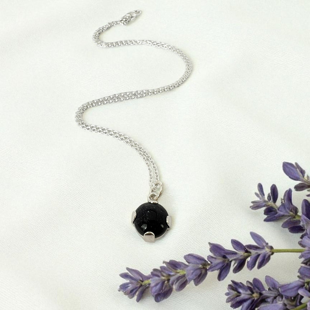 Silver necklace with adeep blue pendant on a white background with lavender flowers.