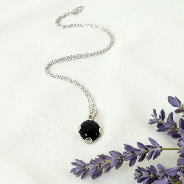Silver necklace with adeep blue pendant on a white background with lavender flowers.