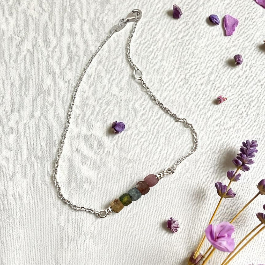 Silver bracelet with colorful beads on a white background with lavender flowers.