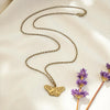 Gold butterfly necklace on a beige surface with purple flowers