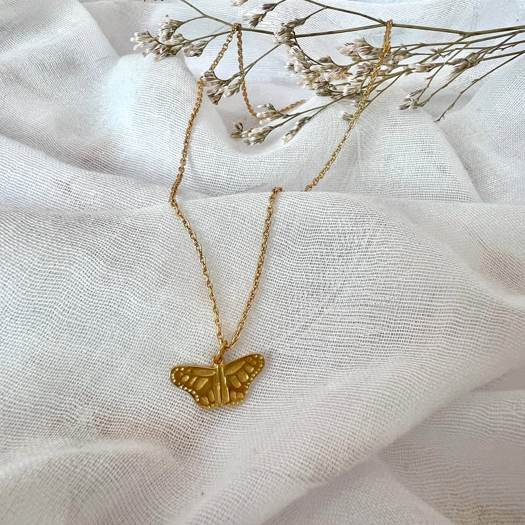 Gold butterfly necklace on a white fabric background