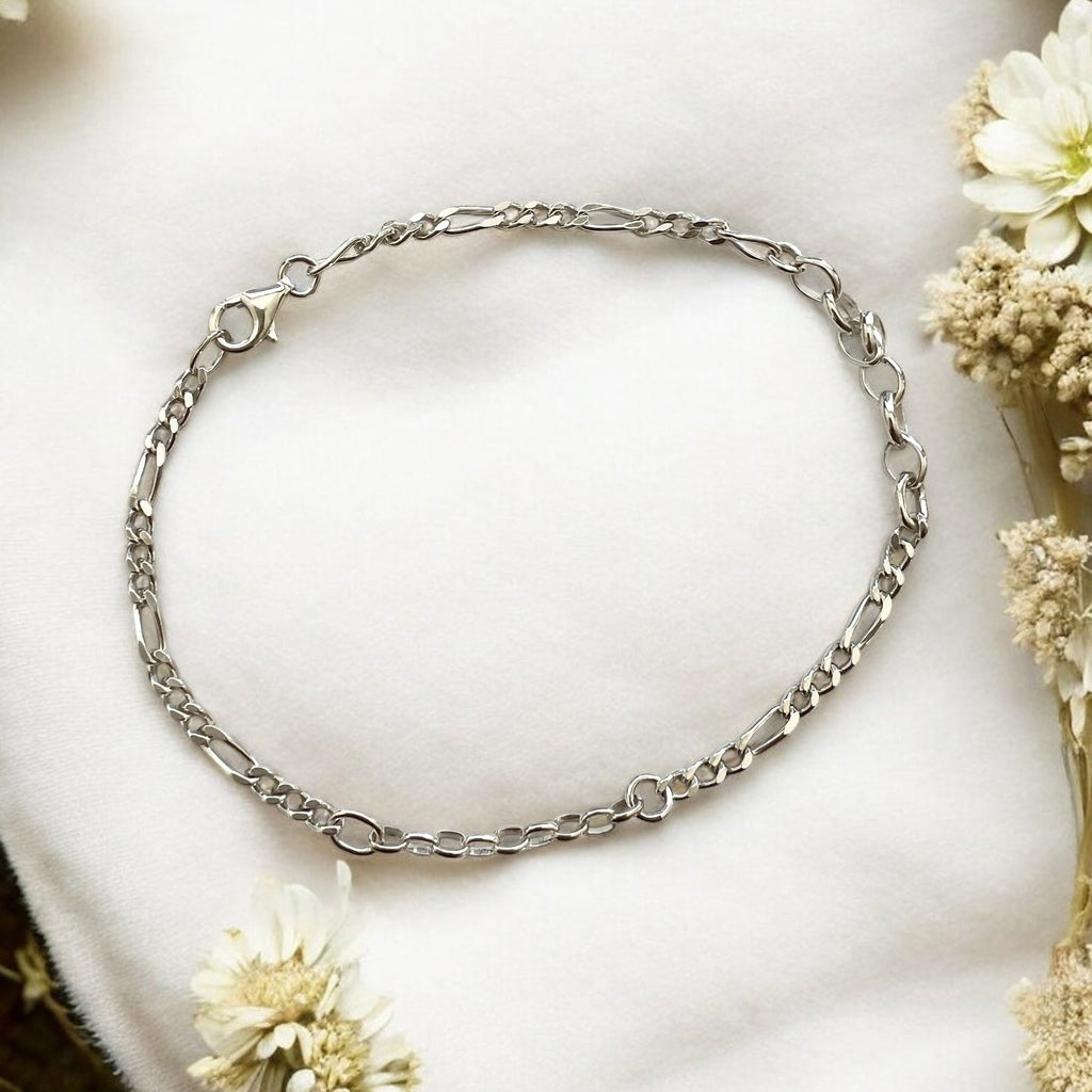 Silver chain bracelet on a white surface with flowers around
