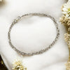 Silver chain bracelet on a white surface with flowers around