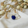 Silver ring with a blue gemstone on a white fabric background with flowers.