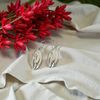 Silver Pohutukawa leaf earrings on a beige fabric with red flowers in the background